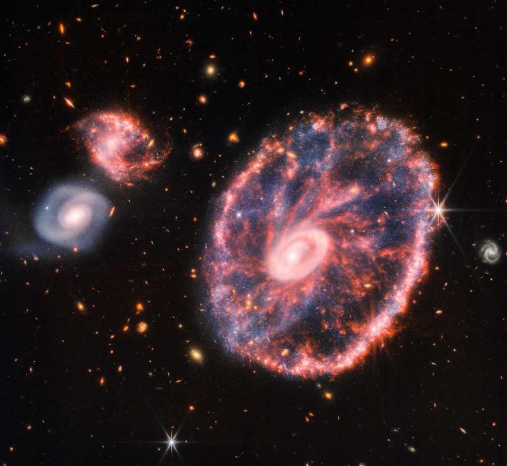 Detrás de la Rueda de Carro brillan otras dos galaxias más pequeñas; además se puede ver otras estructuras. Foto: AFP.