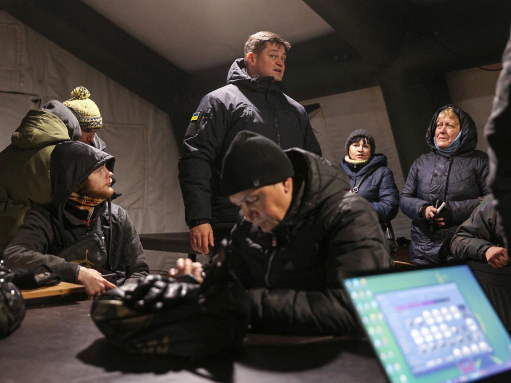 El responsable de la administración regional militar de Jersón, Yaroslav Yanushevich (c), habla con unos habitantes de Jersón en un Punto de Invencibilidad, donde pueden calentarse, cargar sus dispositivos y usar internet, el 5 de diciembre de 2022. Foto: AFP.
