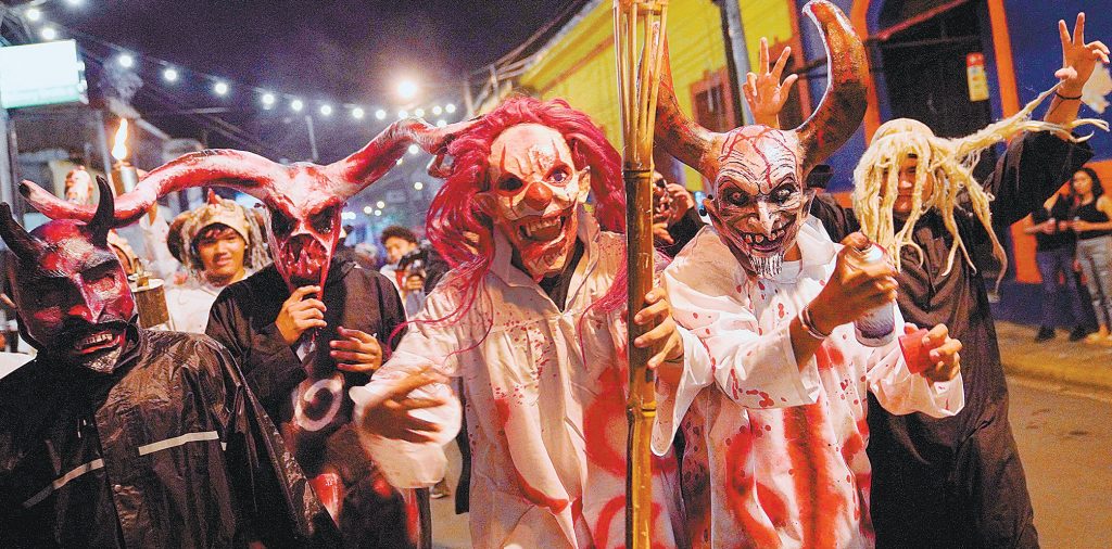 Con máscaras tradicionales y tintes modernos posan para foto en el festival.