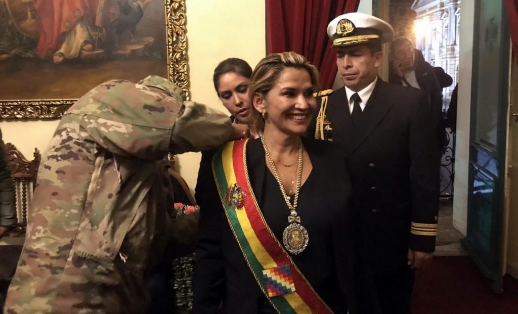 Un jefe militar "arregla" la banda presidencial a la mandataria proclamada Jeanine Áñez, en 2019.